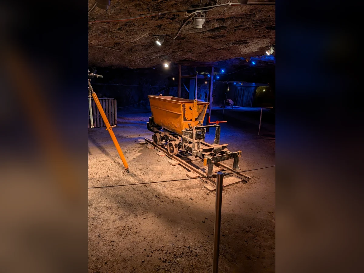 Orangefarbener Grubenwagen auf schmalen Schienen in einer unterirdischen Felskammer