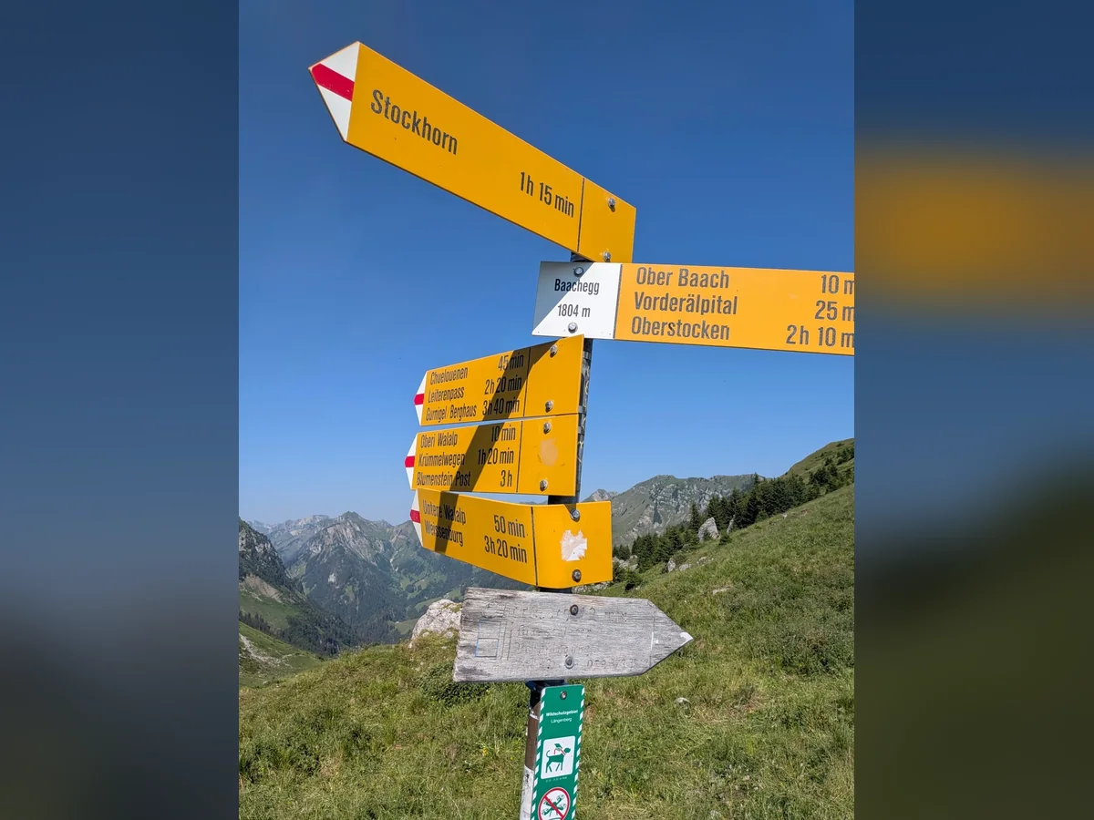 Gelber Wanderwegweiser mit Richtung Stockhorn vor alpiner Berglandschaft