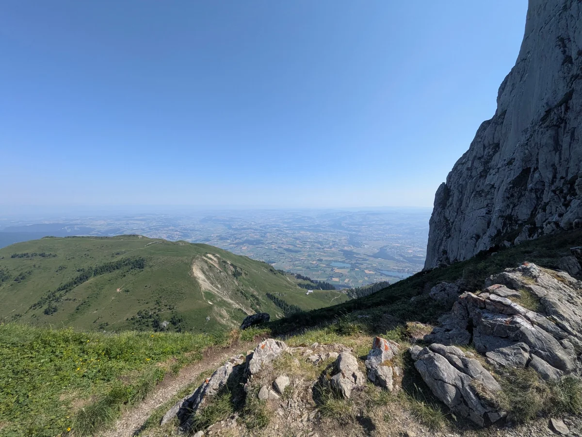 Felsiger Bergweg unter einer steilen Felswand mit weitem Blick ins Tal