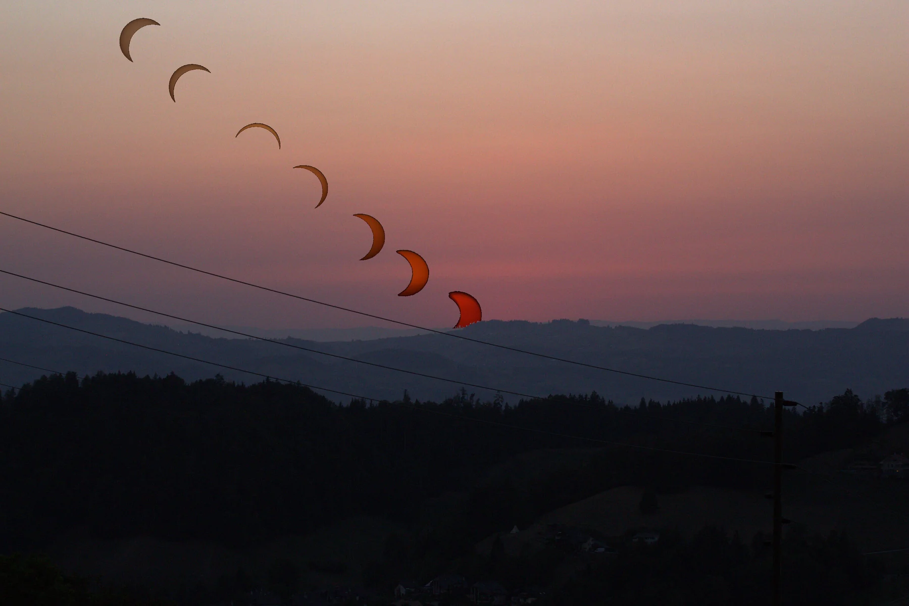 Sieben vergrössert dargestellte Phasen der partiellen Sonnenfinsternis über der abendlichen Landschaft